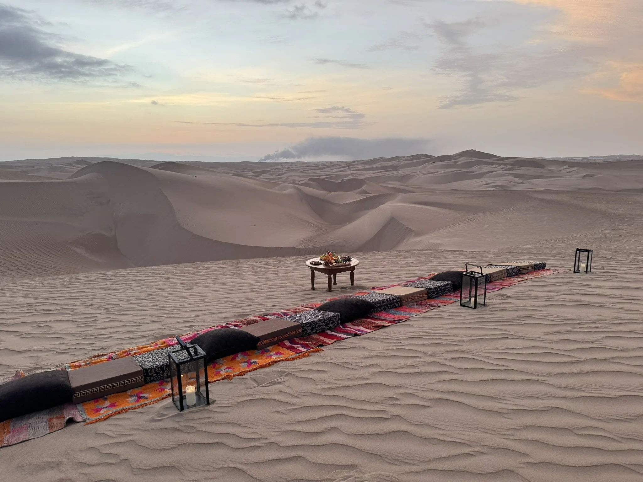 images of blankets and pillows set up for an evening picnic on sand dunes