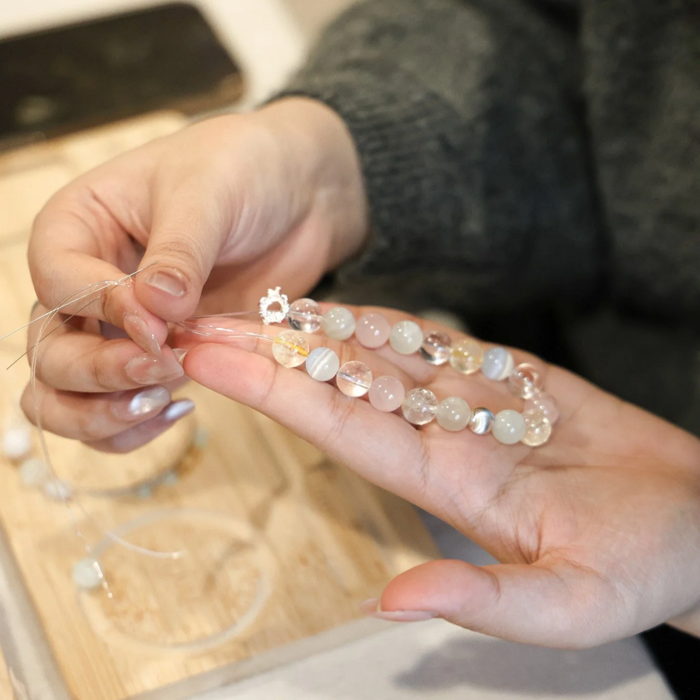 Person stringing a beaded necklace with round, semi-transparent beads using a needle and thread.