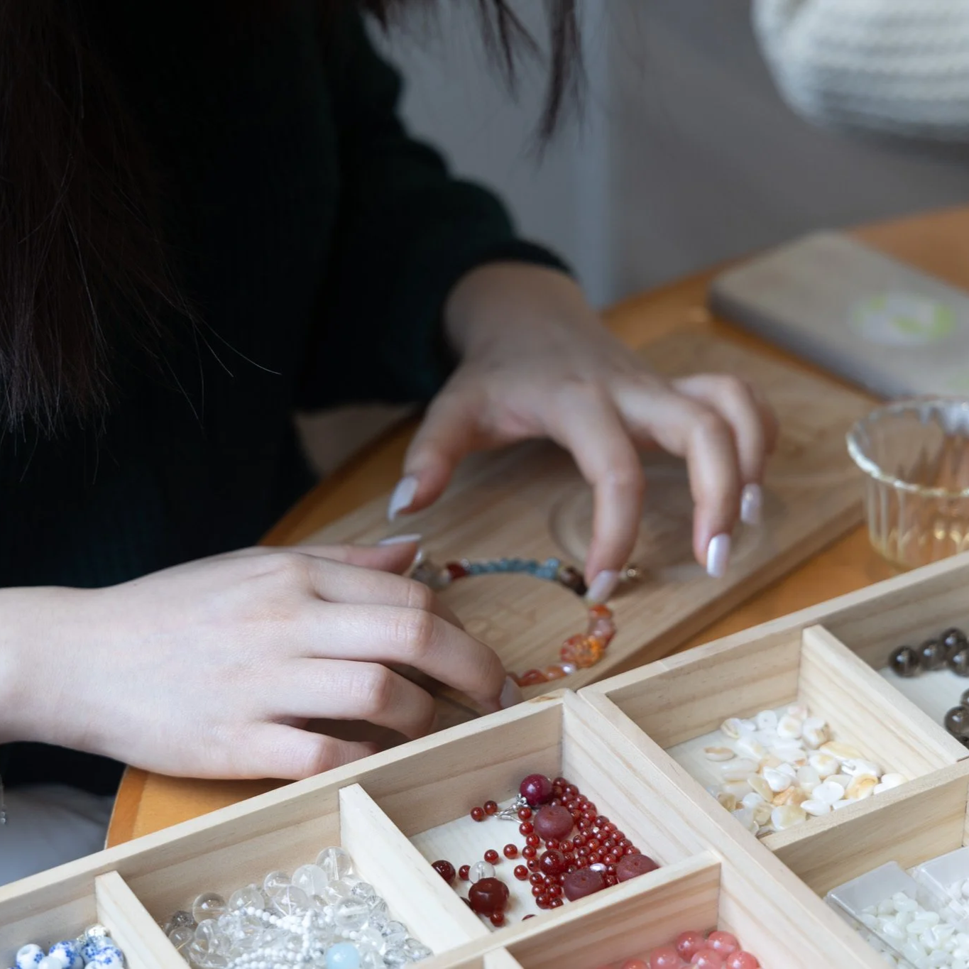 Person making jewelry with beads and jewelry supplies on a wooden table.