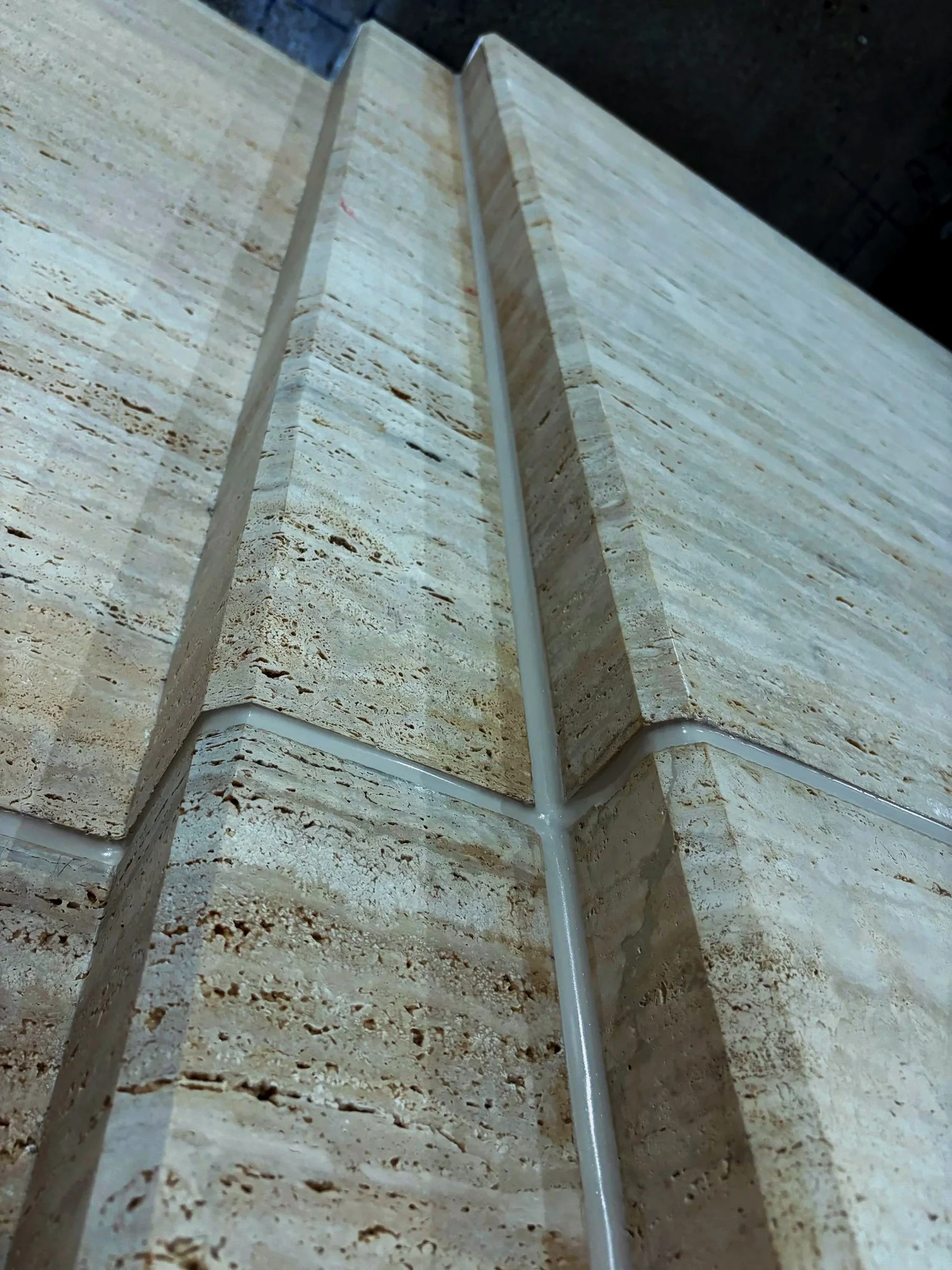 Tooled sealant bead running vertically and horizontally across travertine stone panel joints, meeting at a clean intersection