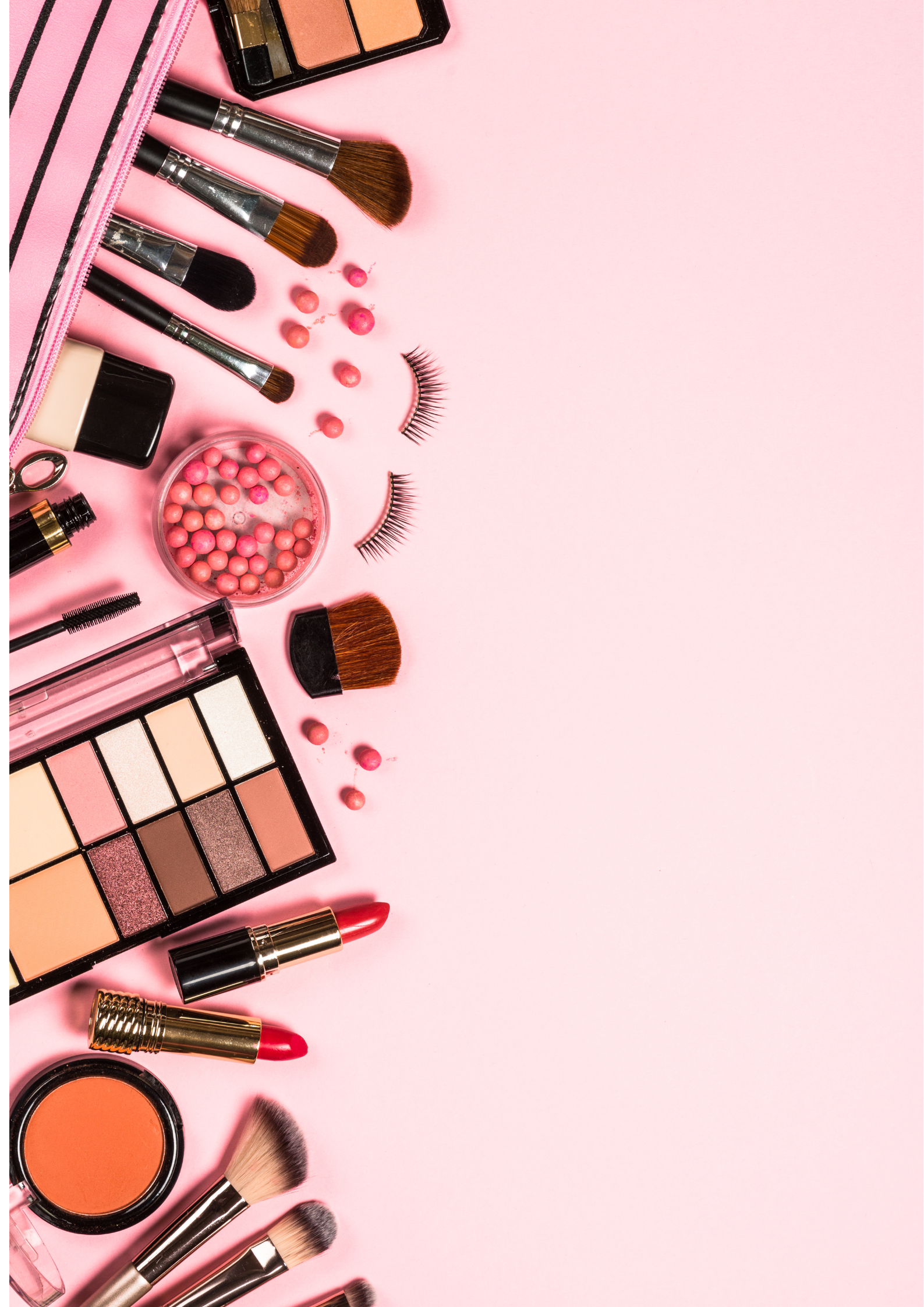 a flat lay of makeup products spead out onto a pink surface includes eyelashes, makeup brushes and palettes