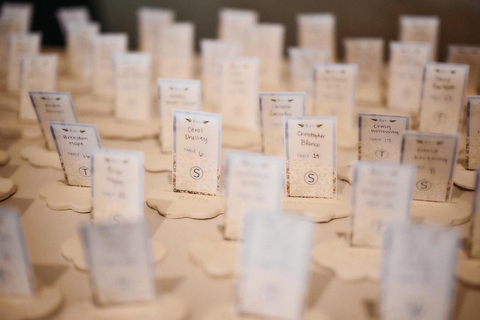 Table place cards arranged in rows, with handwritten names and table numbers, at an event or wedding reception.