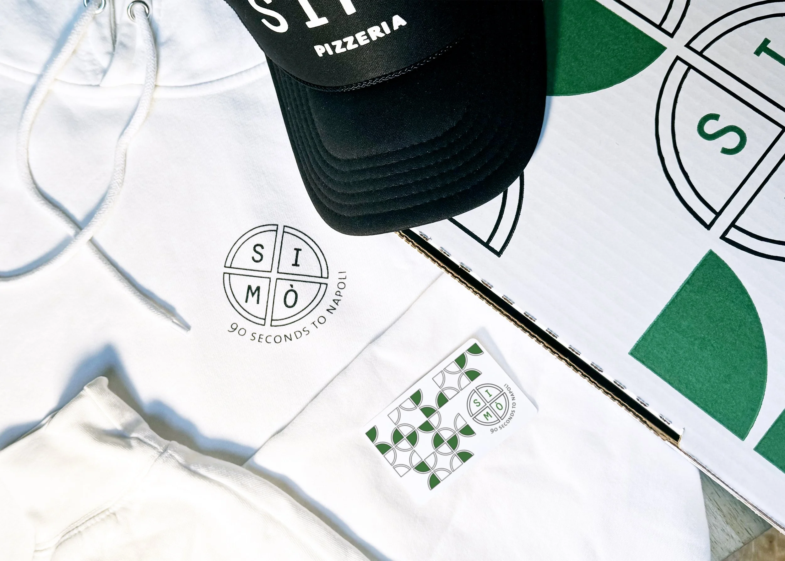 A white hoodie, green and white pizza box, a cap with black and green colors, and printed materials with the logo of SÌMÒ, a pizza place in New York City, and the phrase '90 Seconds to Napoli'.
