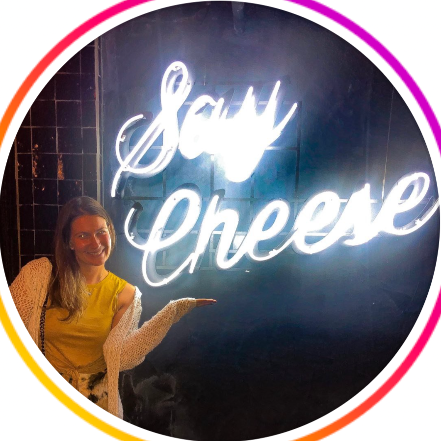 Woman smiling and pointing at a neon sign that reads "Say Cheese" in cursive font