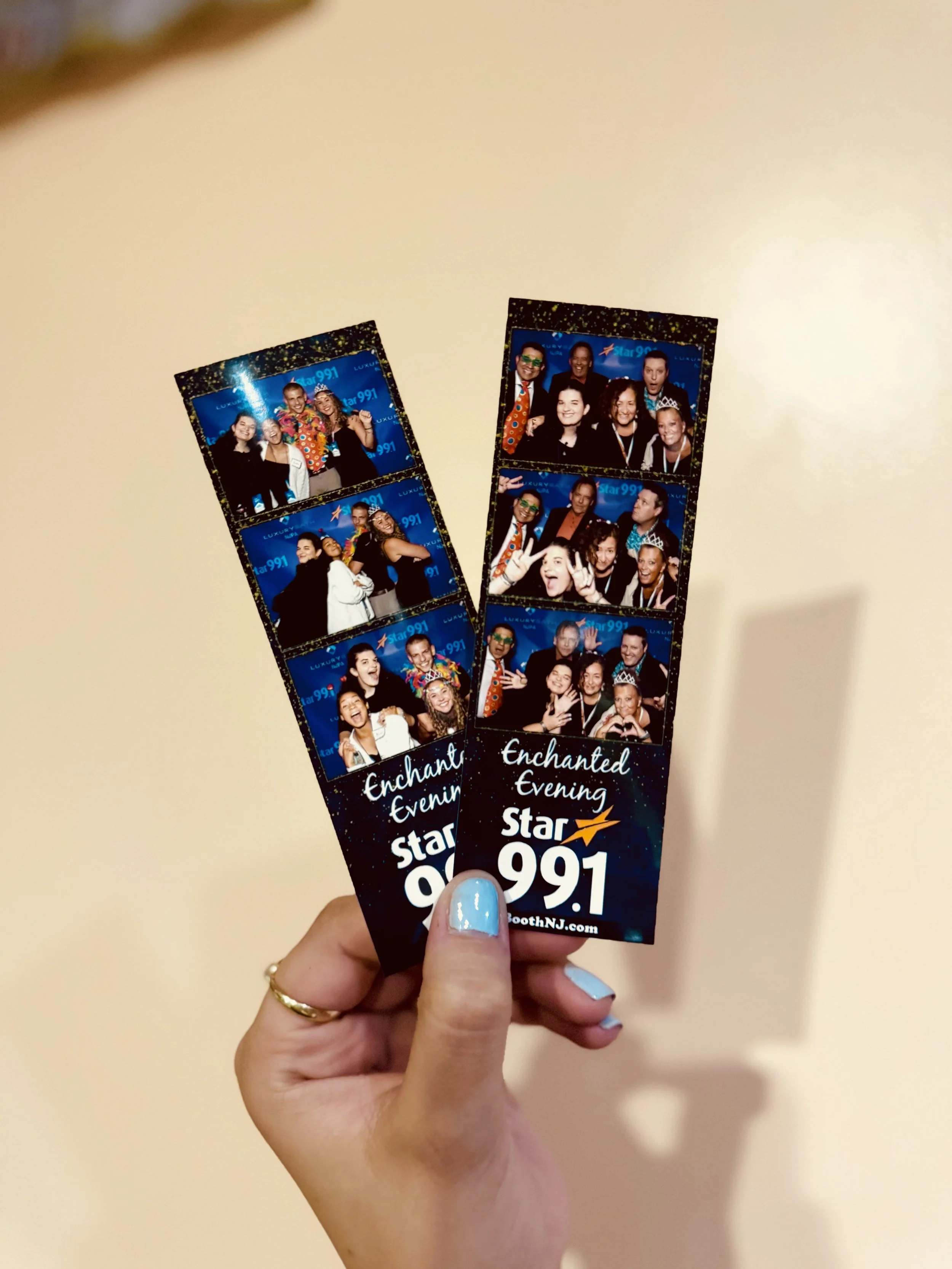 Hand holding two photo booth strips with group of people at an event, with a starry night background and text 'Enchanted Evening Star 99.1'.