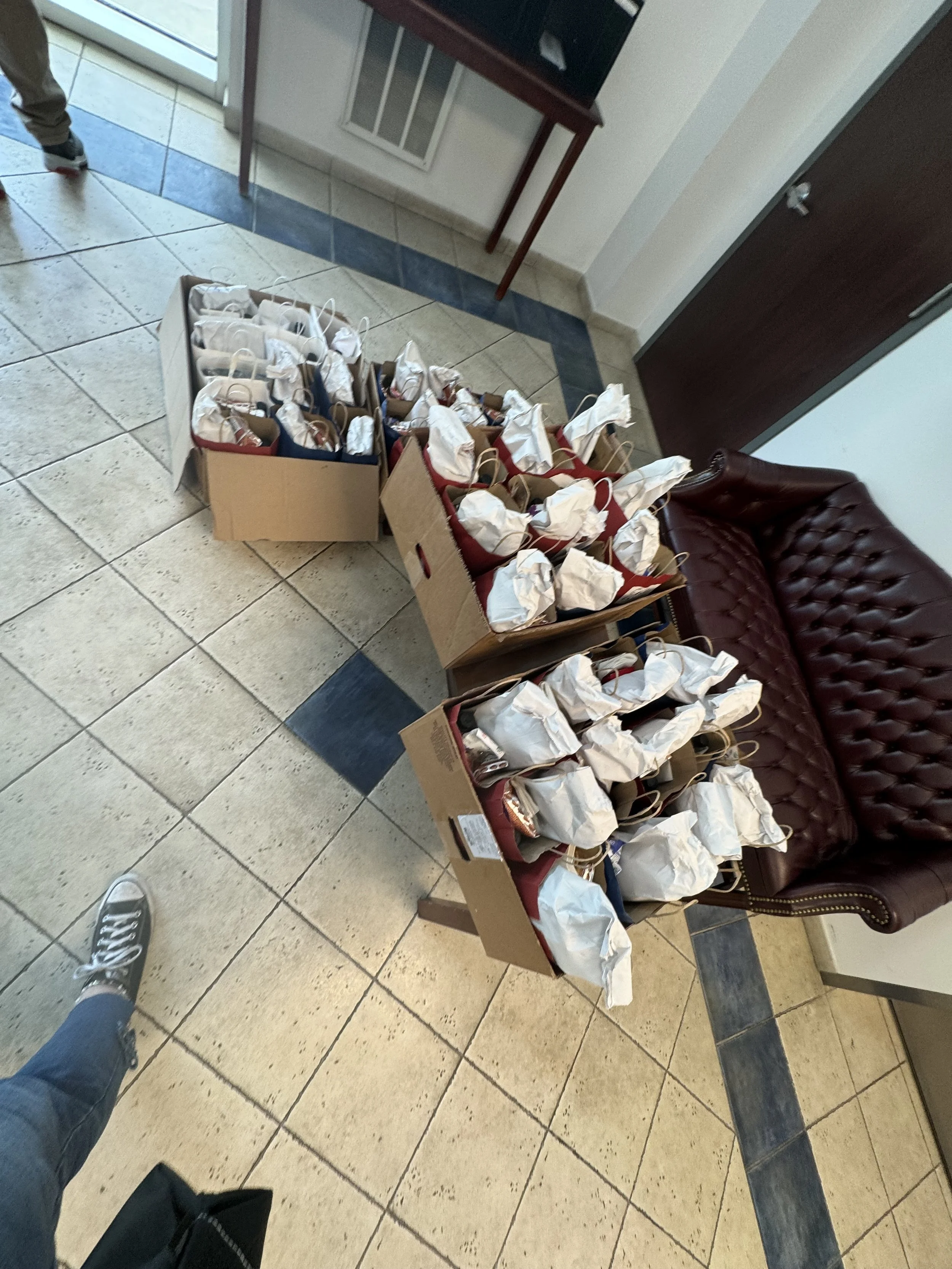 Several boxes filled with wrapped lunches placed on a small table inside a building, near a leather couch and a door.