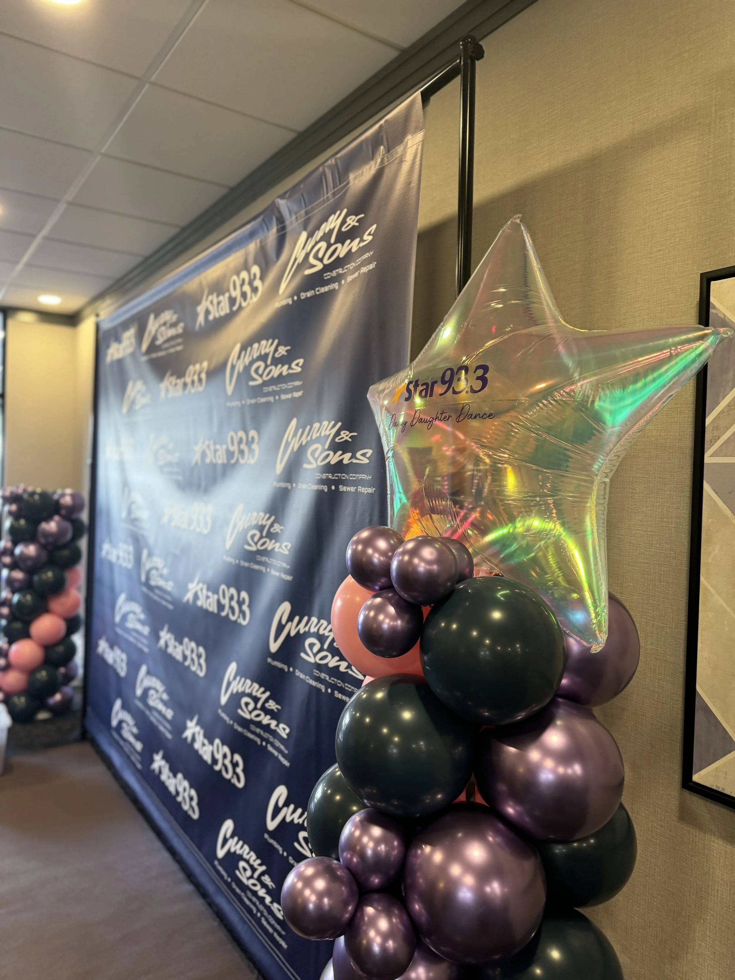 Decorative balloon arrangement with a star-shaped metallic balloon and smaller cluster of purple and pink balloons, set against a backdrop with 'Cunny & Sons' and 'Star 93.3' logos.