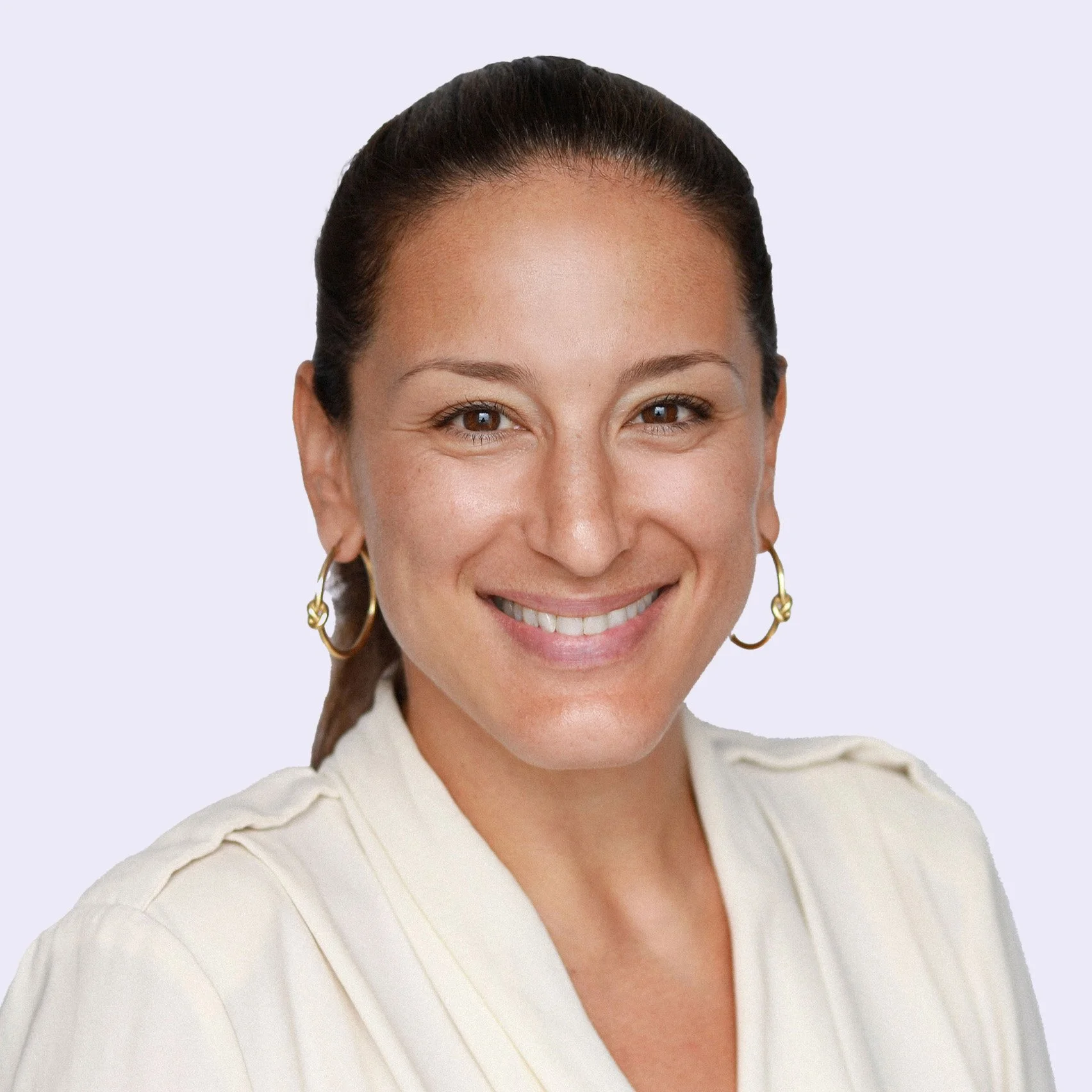 A smiling woman with brown hair tied back, wearing a cream-colored shirt and gold hoop earrings, against a light background.