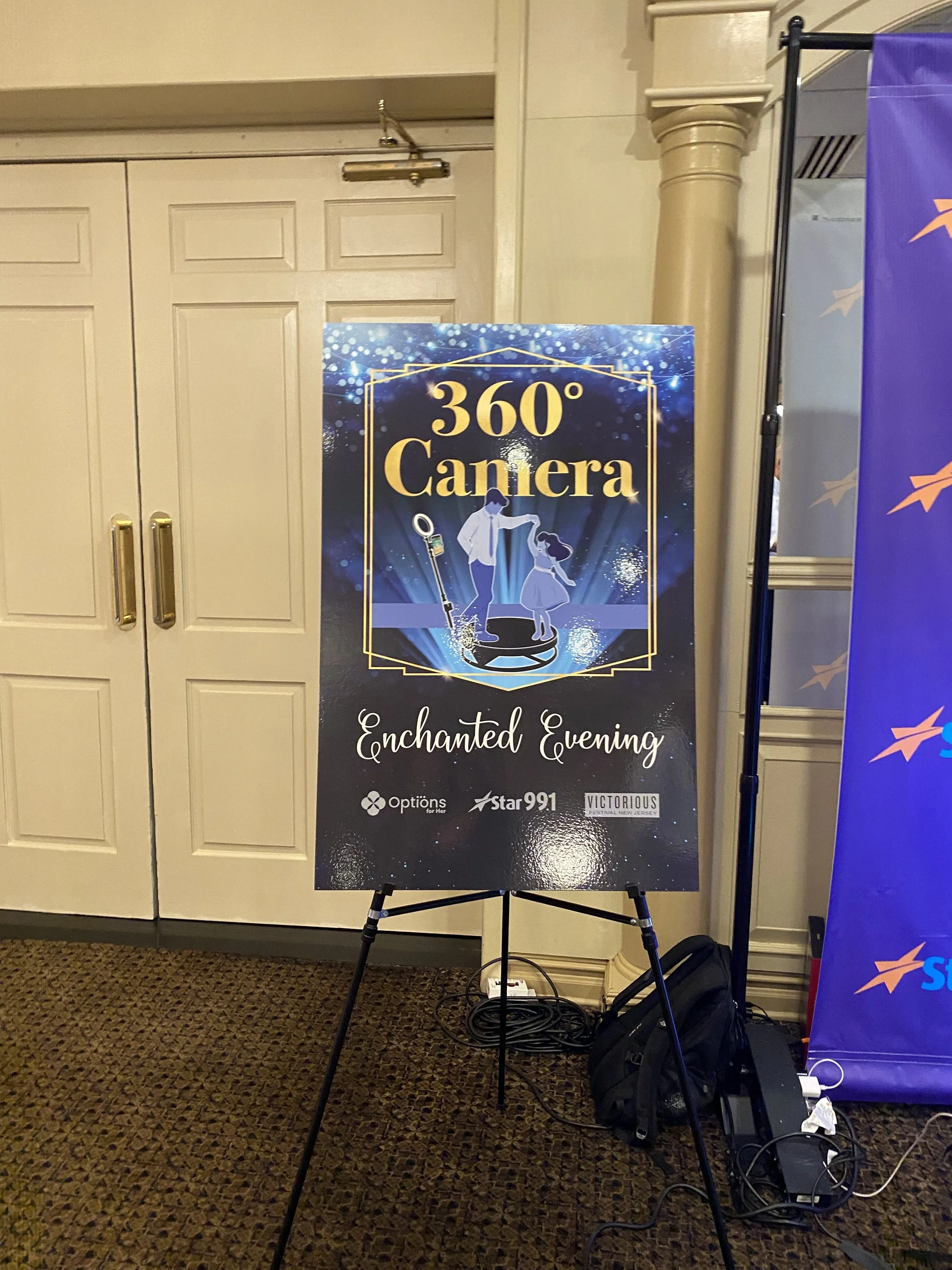 Event sign for '360° Camera Enchanted Evening' with illustrations of a man and a girl on a circular platform, set against a starry background.