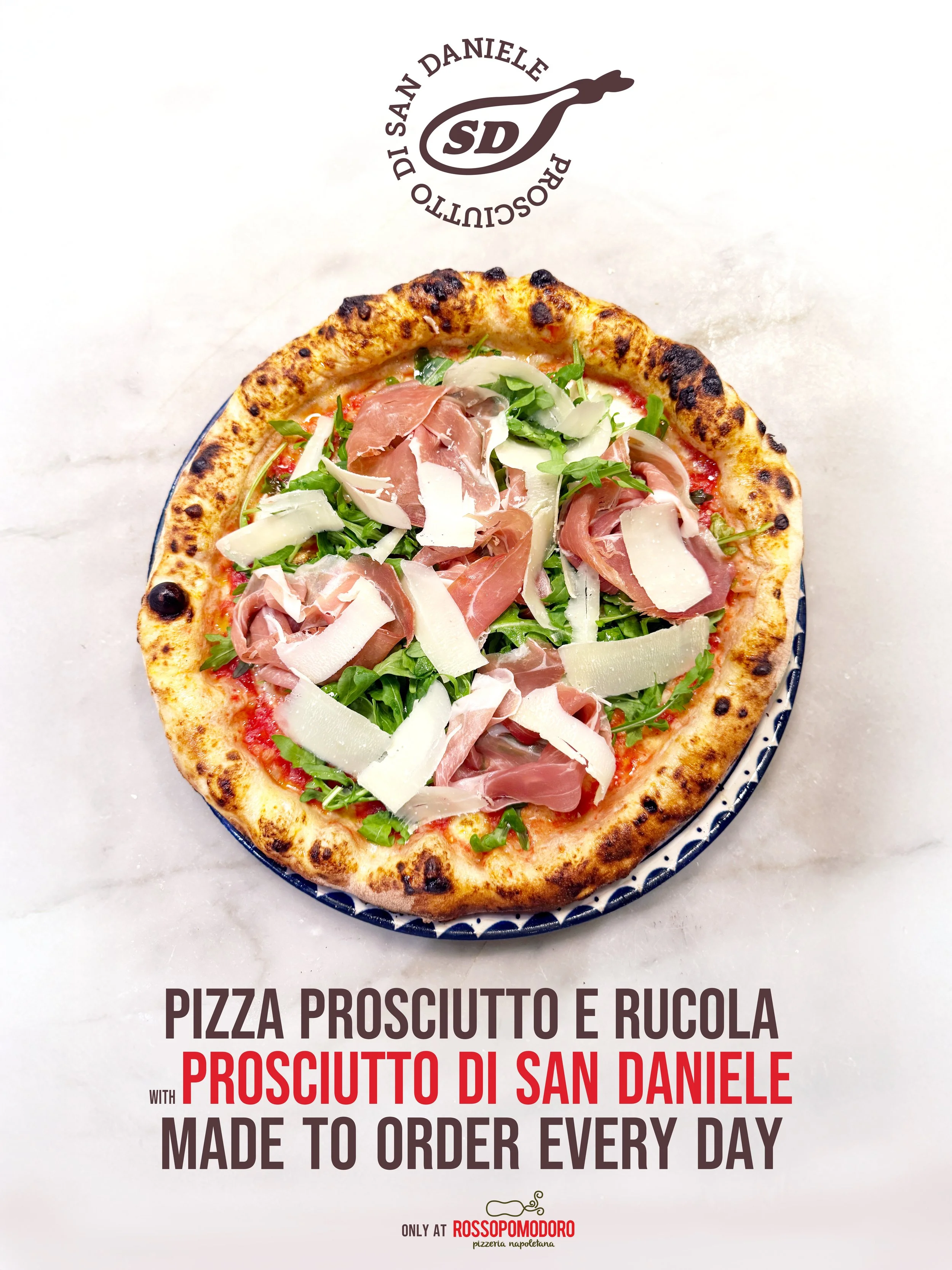 A pizza topped with prosciutto and arugula, served on a patterned plate. The background has the restaurant's logo and promotional text about the pizza.