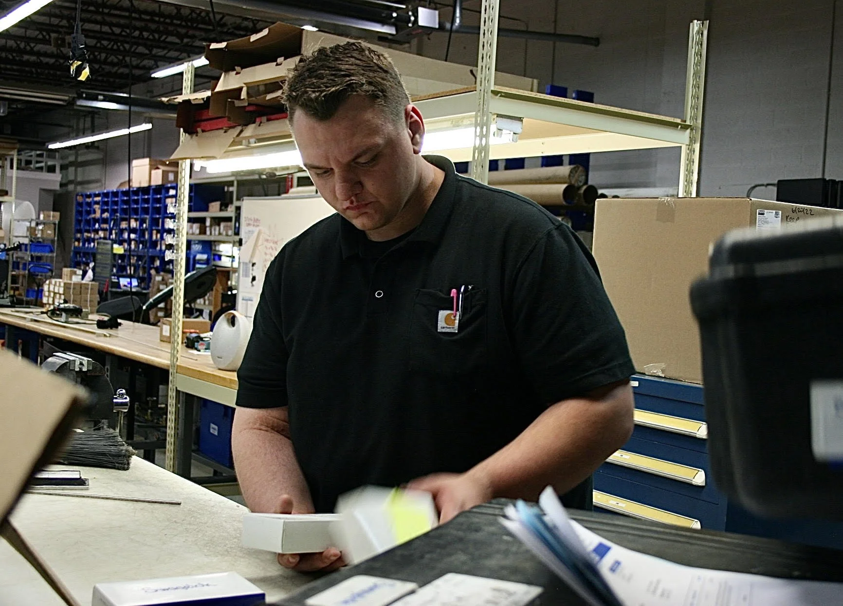 A man working in a warehouse or storage area, sorting through packages or boxes at a cluttered workbench.
