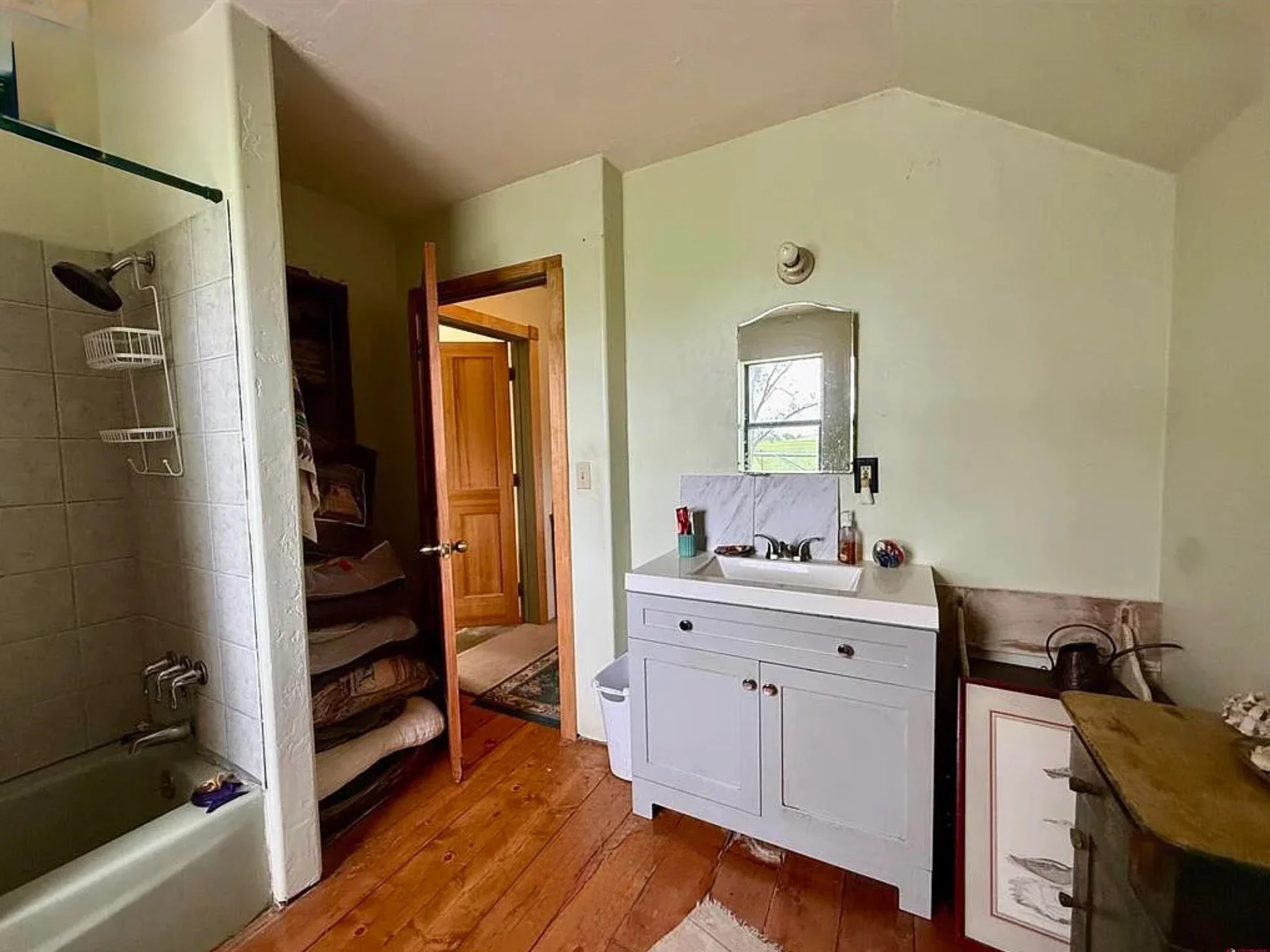 Bathroom with white vanity, sink, mirror, bathtub, tiled shower, and wooden floors