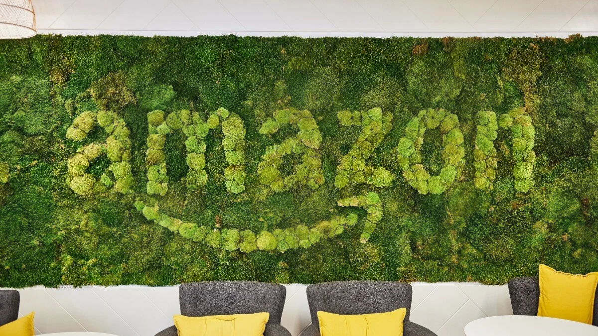 Green moss wall with the numbers 2020 spelled out in moss and a smiley face in moss, with yellow pillows and gray chairs below.