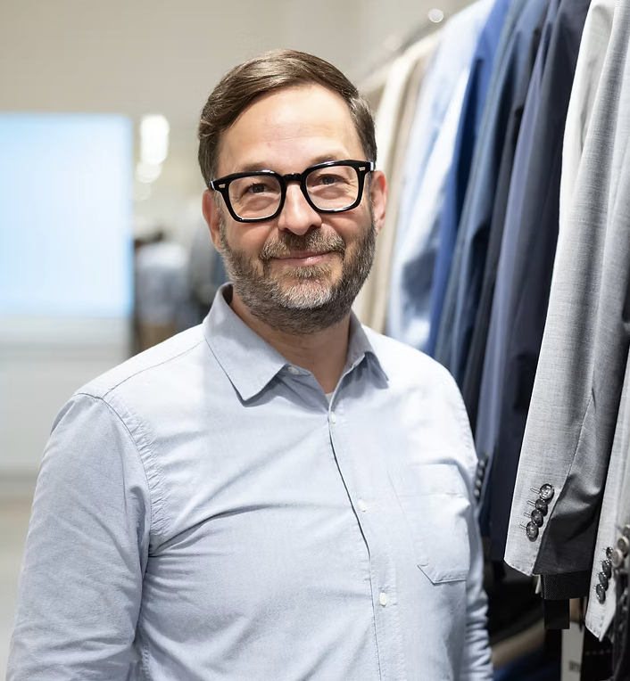 Mann in Brille vor Kleidungsauswahl in einem Geschäft