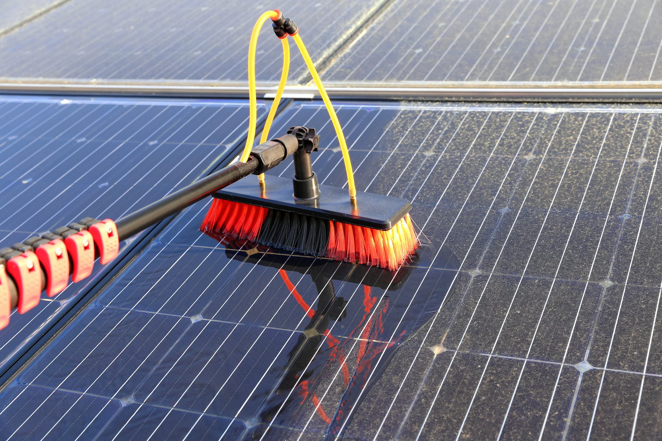 Close-up of a broom sweeping water off solar panels outdoors.