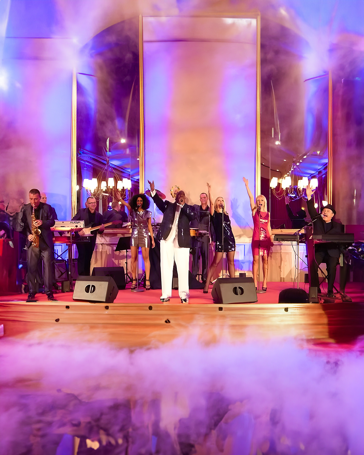 Musiker und Sänger auf einer Bühne während einer Live-Performance, mit Rauch und buntem Licht, in einem eleganten Veranstaltungsraum.