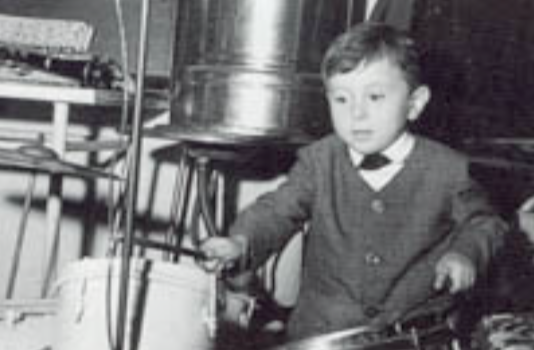 Schwarz-Weiß-Foto eines Jungen in einem Anzug, der an einem Fahrrad sitzt.