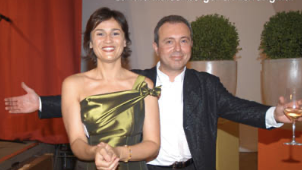 Ein Mann und eine Frau feiern zusammen, der Mann hält ein Glas Wein, beide tragen elegante Kleidung.