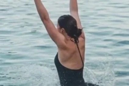 Woman in a swimsuit swimming in open water with her arms raised.