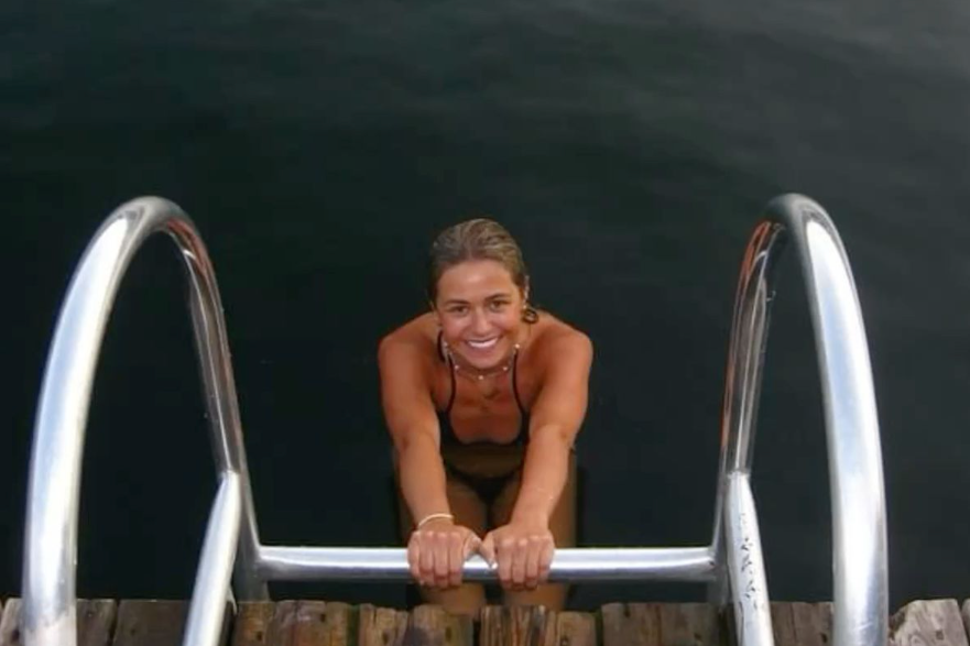 Woman smiling while climbing out of a swimming pool via a metal ladder.