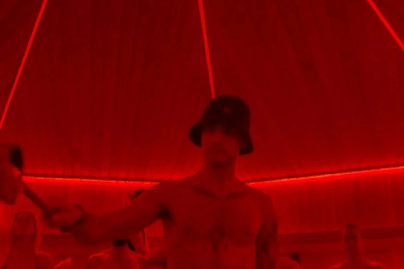 Person with a hat holding a sword in a dimly lit room with red neon lights.