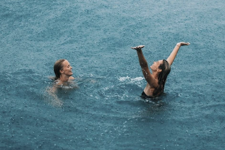 Two women playing in a swimming pool, with one woman raising her arms and the other smiling.