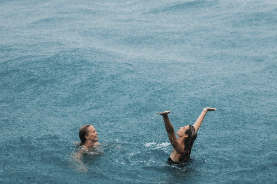 Two women swimming and playing in the ocean, one woman is splashing water in the air.