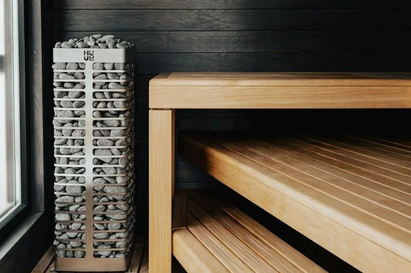A sauna room interior with a wooden bench and a heater filled with sauna stones.
