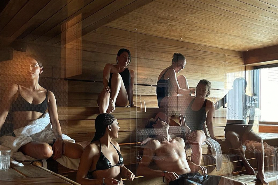 Multiple women relaxing and sitting in a wooden sauna or spa room.