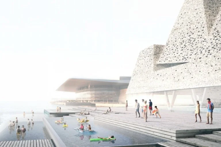 Modern architectural buildings near a waterfront with people walking and children playing, some in the shallow water and on the steps.