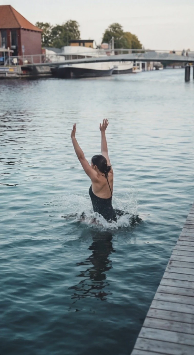 A person in a black swimsuit with long dark hair swimming in a body of water, raising their arms above their head.