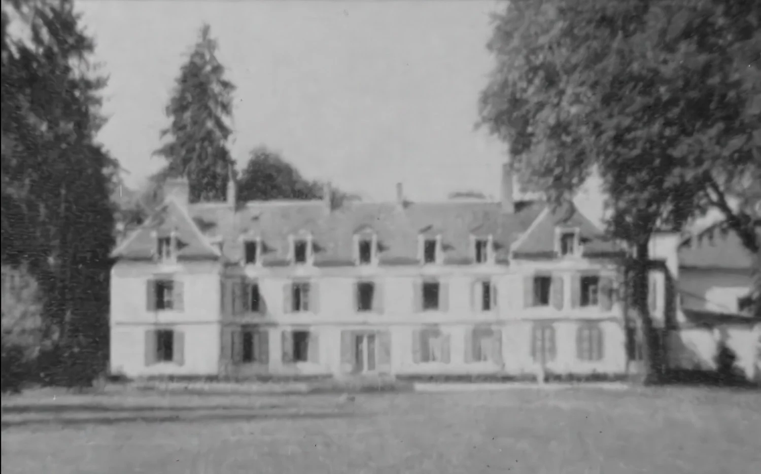 Black and white photo of a large, multi-story house with multiple windows and chimneys, surrounded by trees and a lawn.