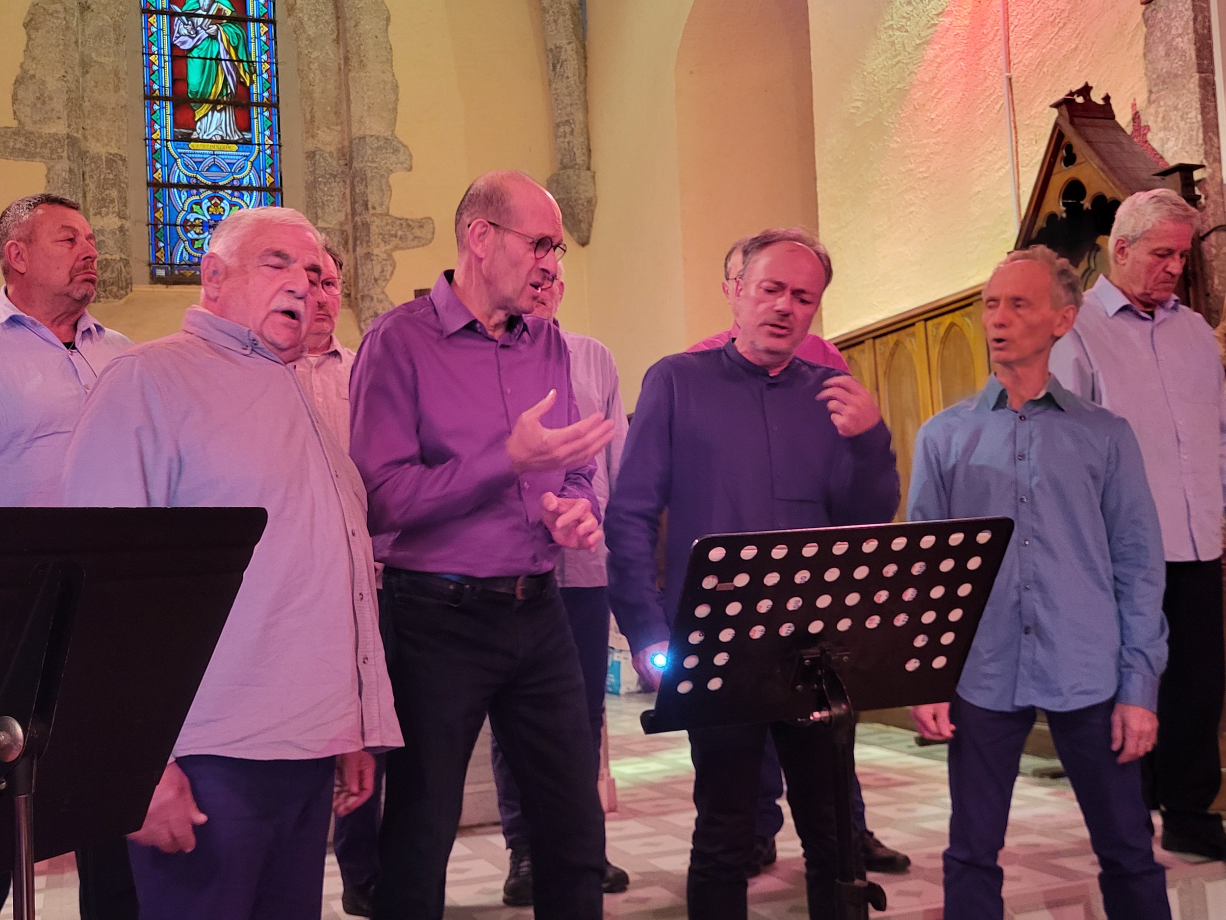 Groupe d'hommes chantant dans une église, avec vitrail coloré en arrière-plan.