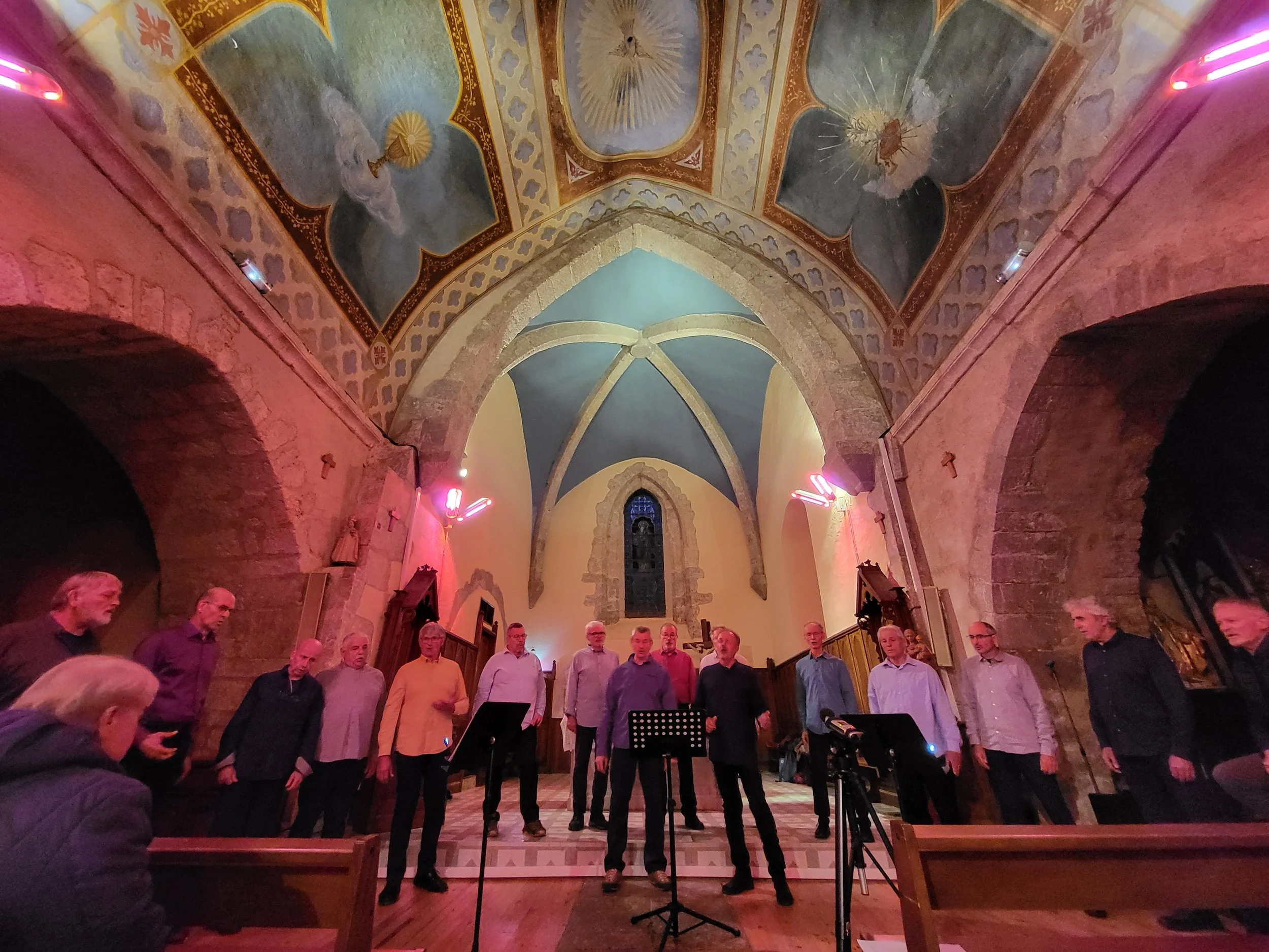 Un groupe de personnes chantant dans une église avec un plafond coloré et des arches en pierre.