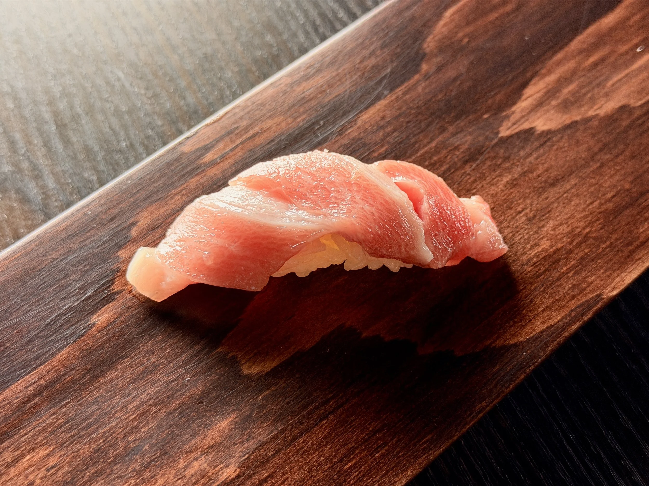 Piece of raw salmon sushi on a wooden serving board.