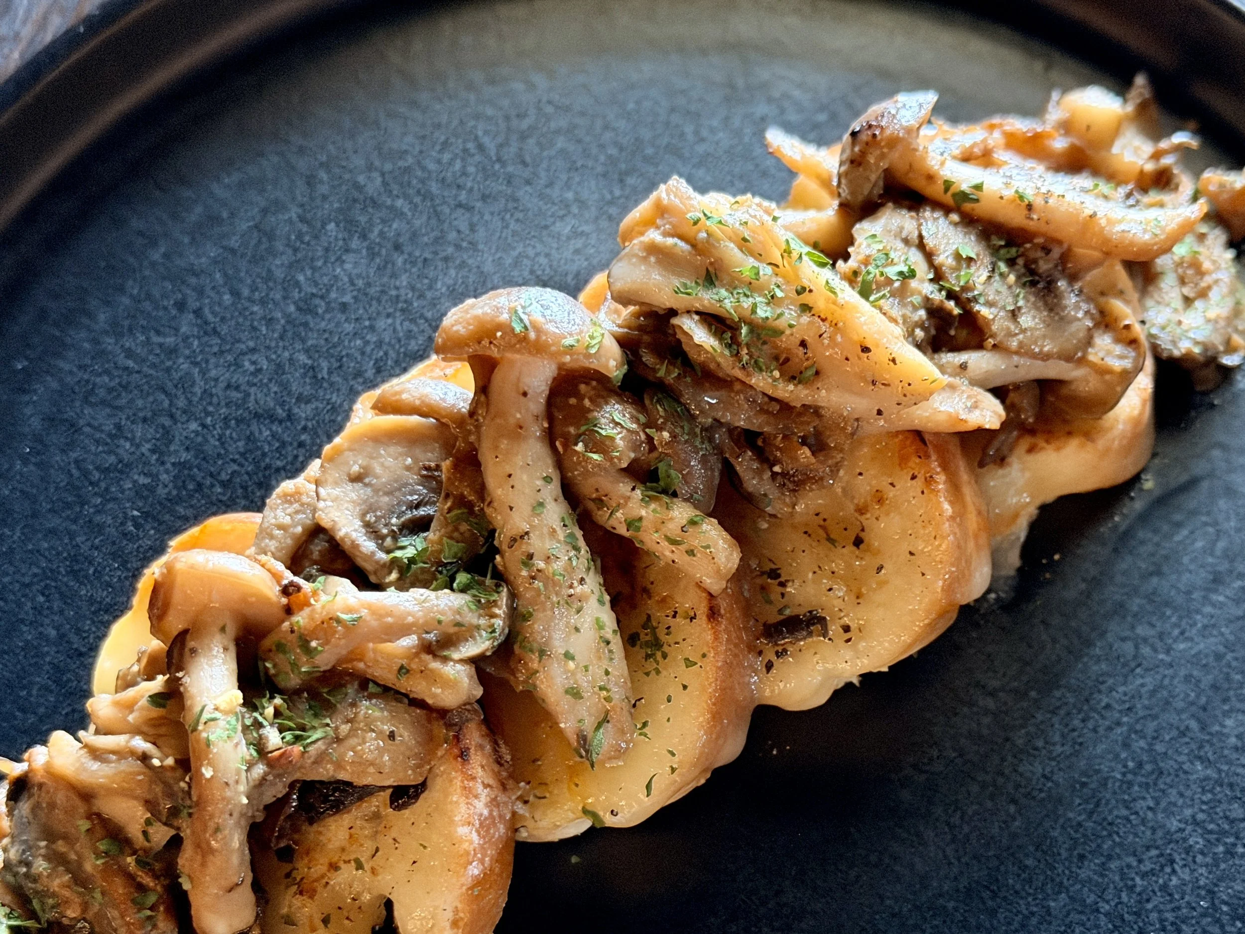 Cooked mushroom and chicken dish garnished with chopped herbs on a black plate.