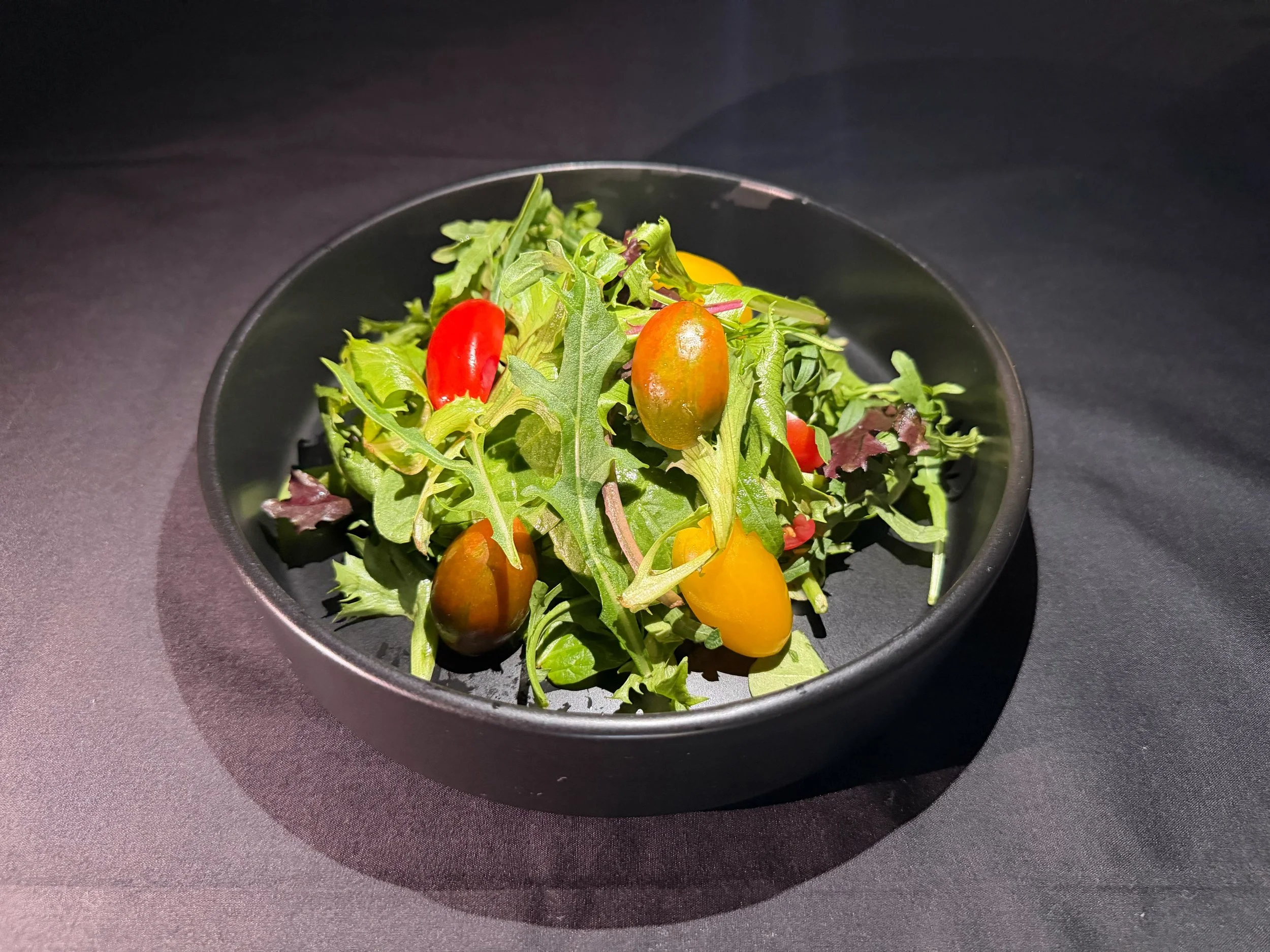 Mixed salad with cherry tomatoes and arugula in a black bowl on a black surface.