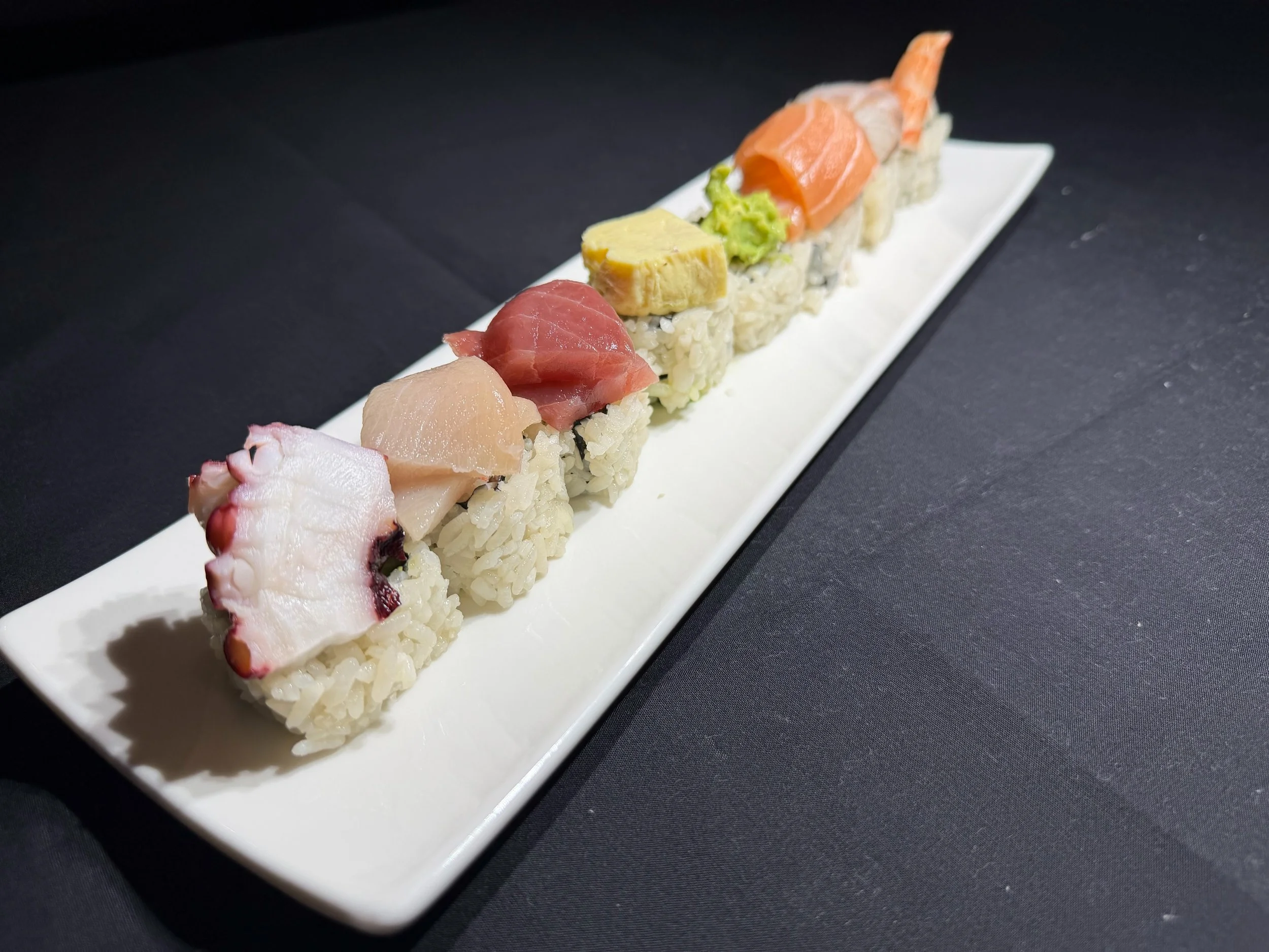 A rectangular plate with assorted sushi rolls on a black surface.