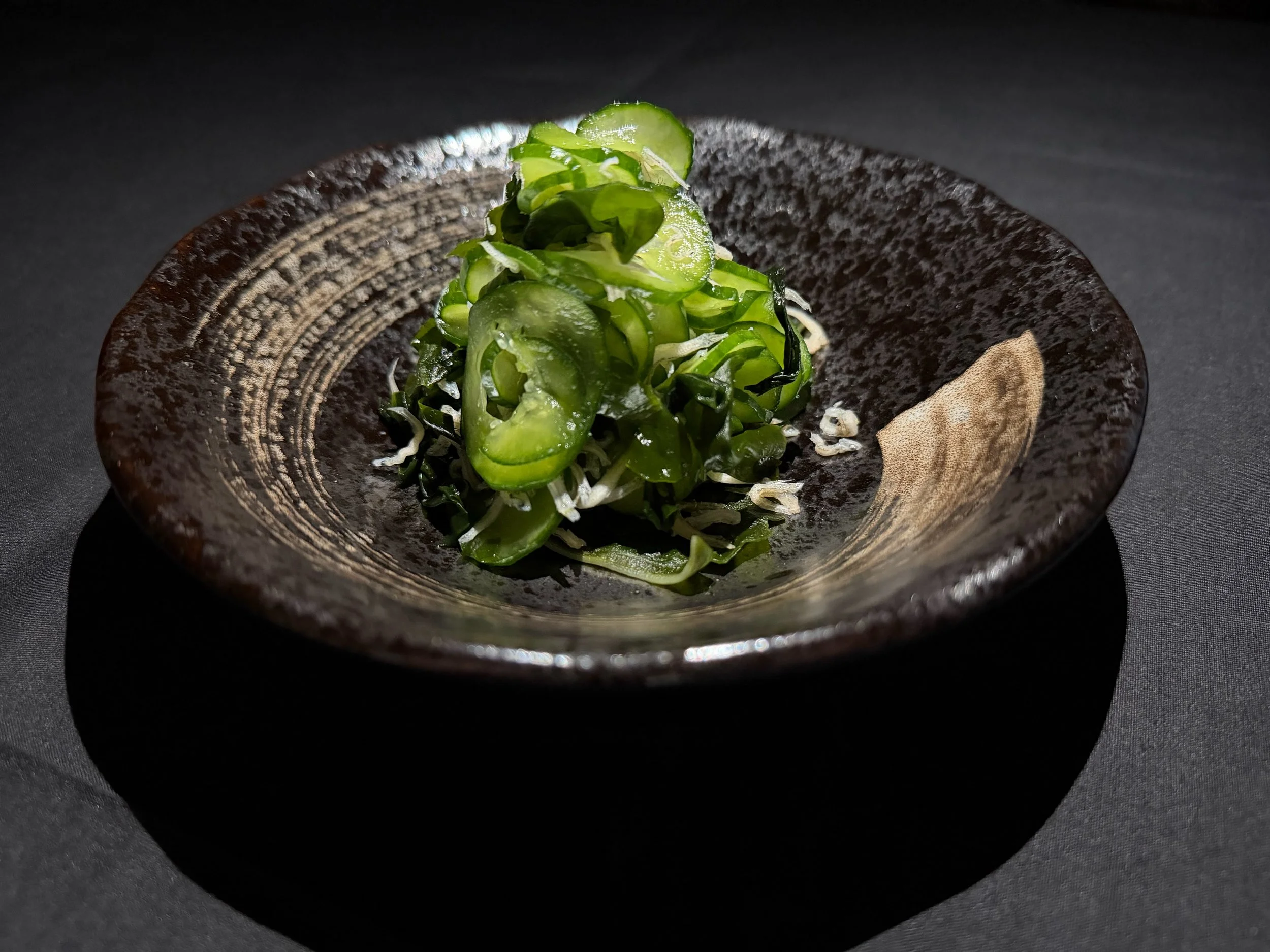 Green seaweed salad on a black textured ceramic plate.
