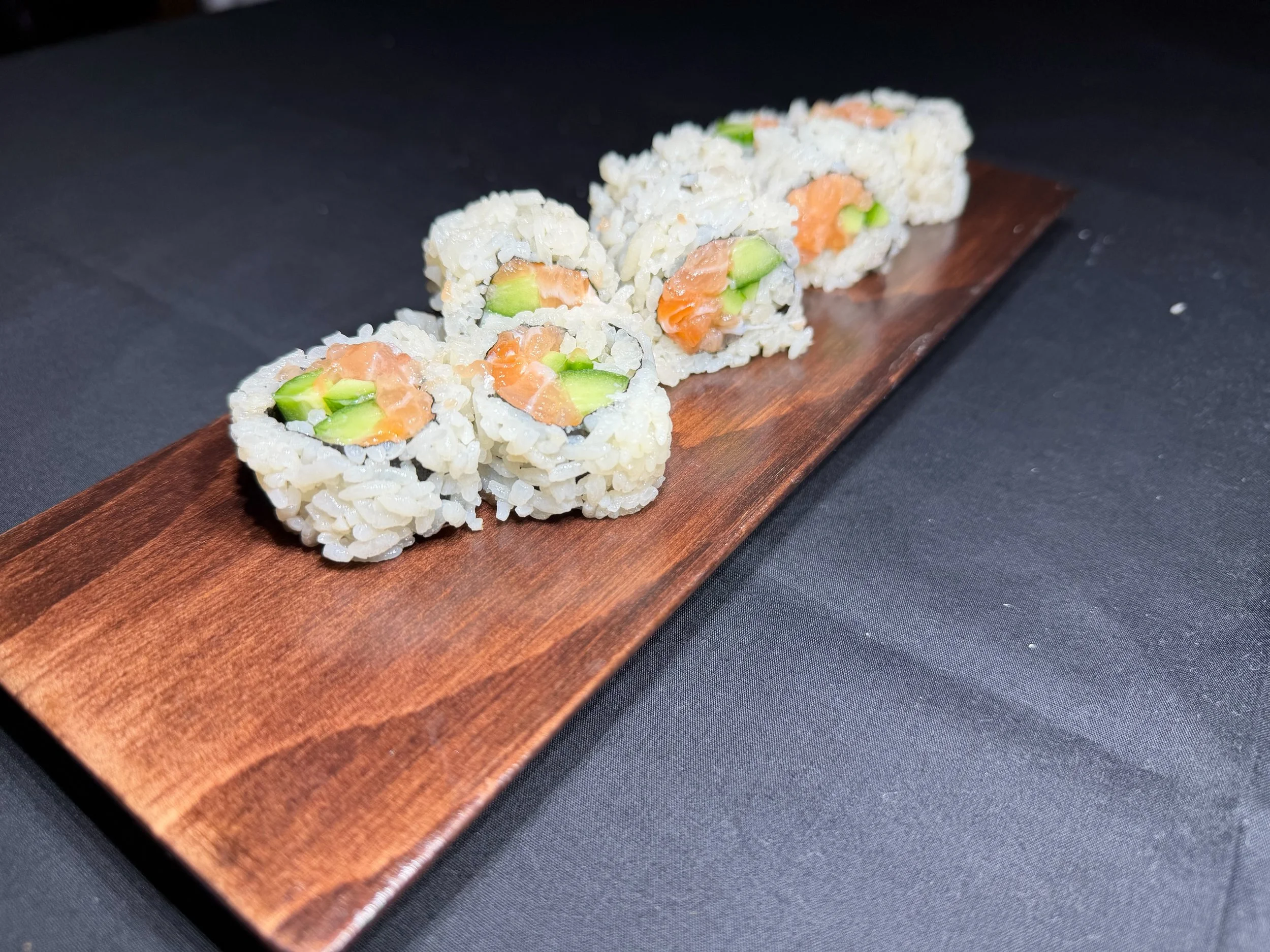 Sushi rolls with salmon and avocado on a wooden serving board.