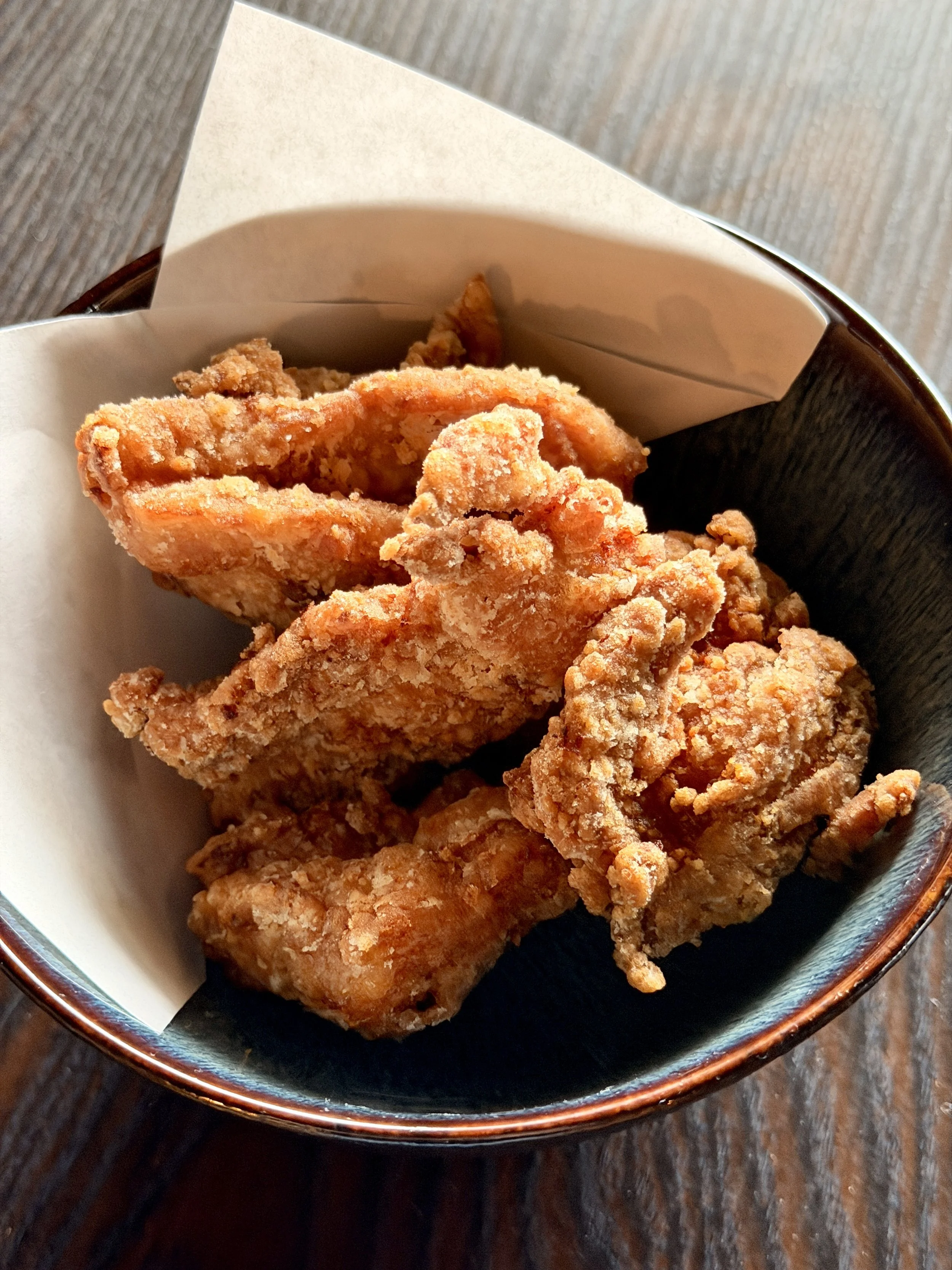 Close-up of fried chicken pieces in a bowl on a dark wooden table.