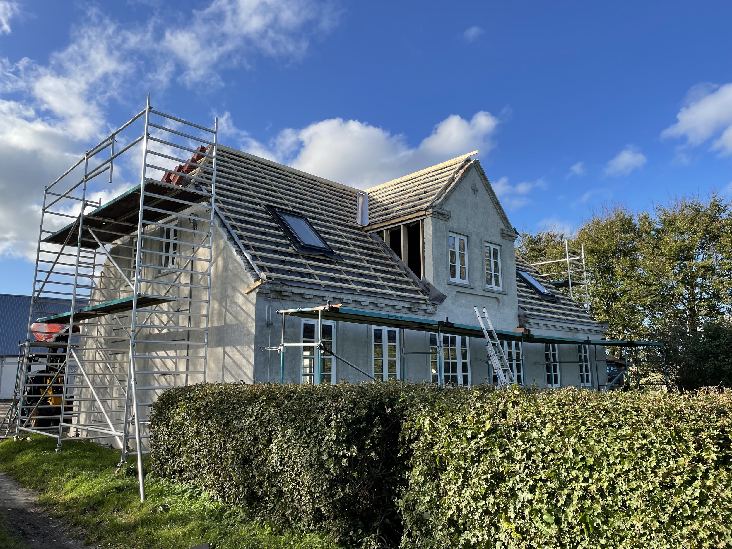 Hus under renovering med stilladser rundt, tagarbejde i gang, blå himmel med skyer.