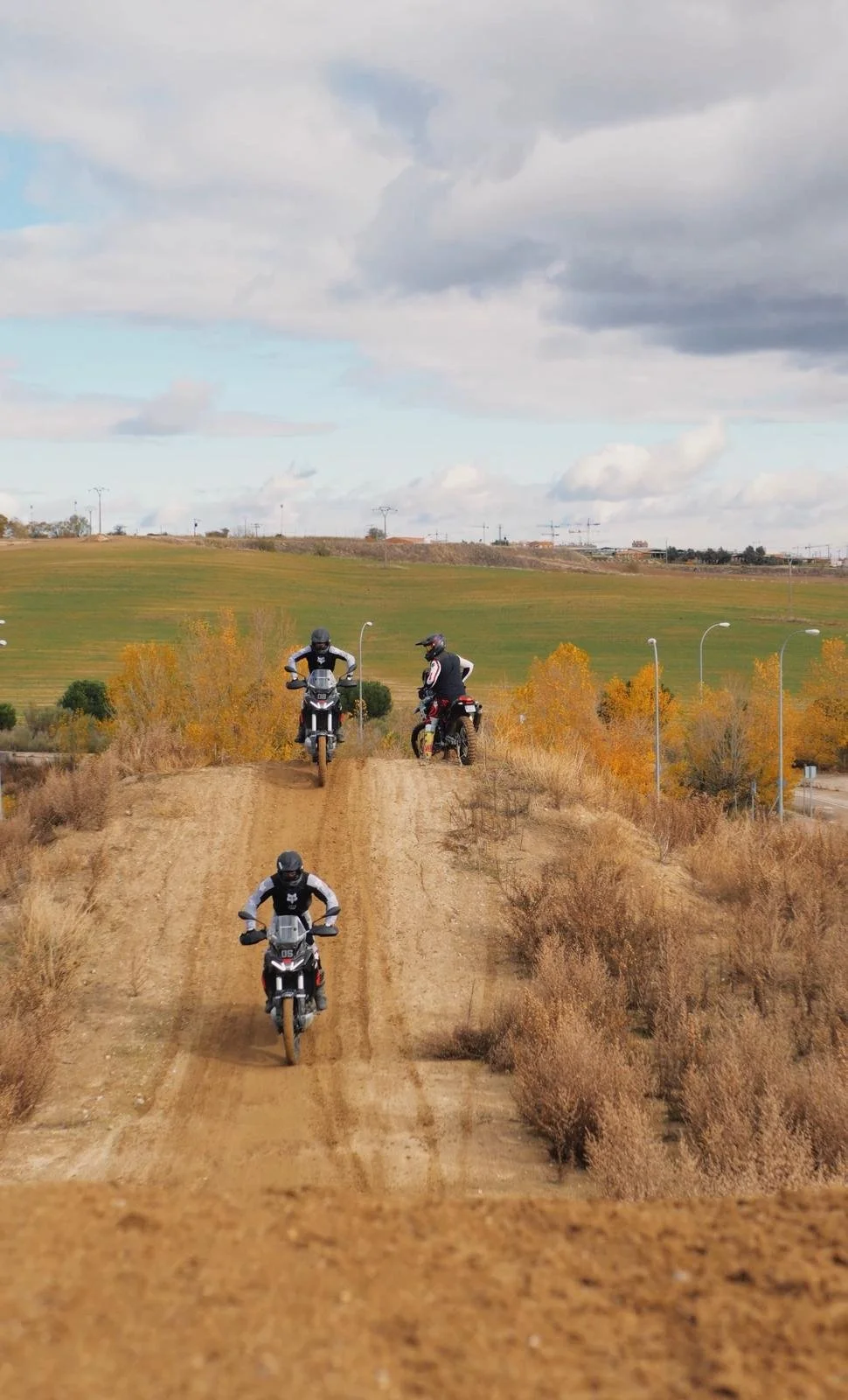 Piloto de motocicleta en vuelo en una pista de tierra con paisaje abierto y árboles.