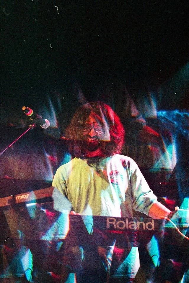Persona tocando un teclado en un escenario con luces de colores y micrófono