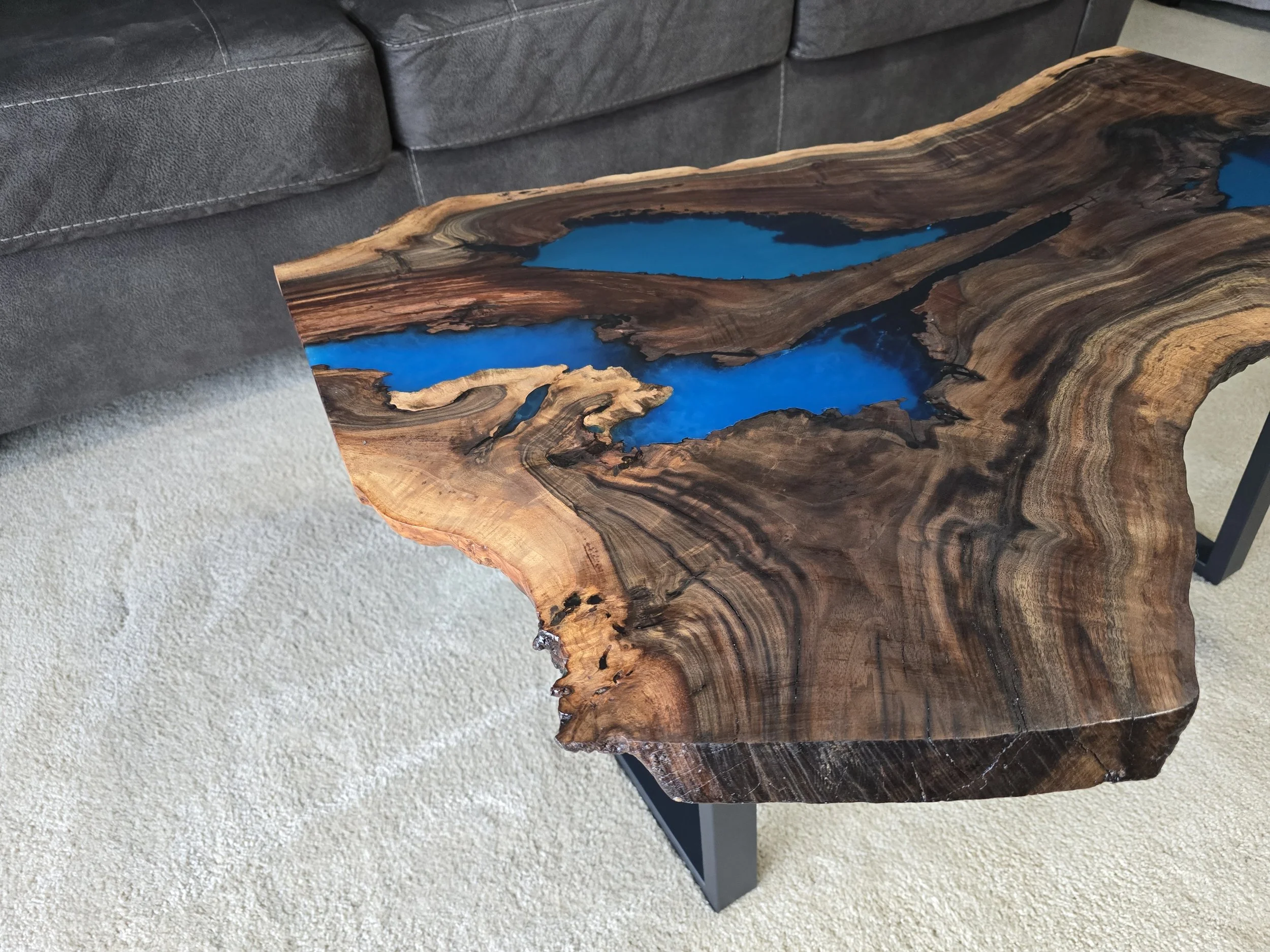 Black walnut coffee table with metal table legs and adjustable feet. Semitransparent blue epoxy fills voids. Measures 18 inches tall, 36 inches long, and 24 inches wide.