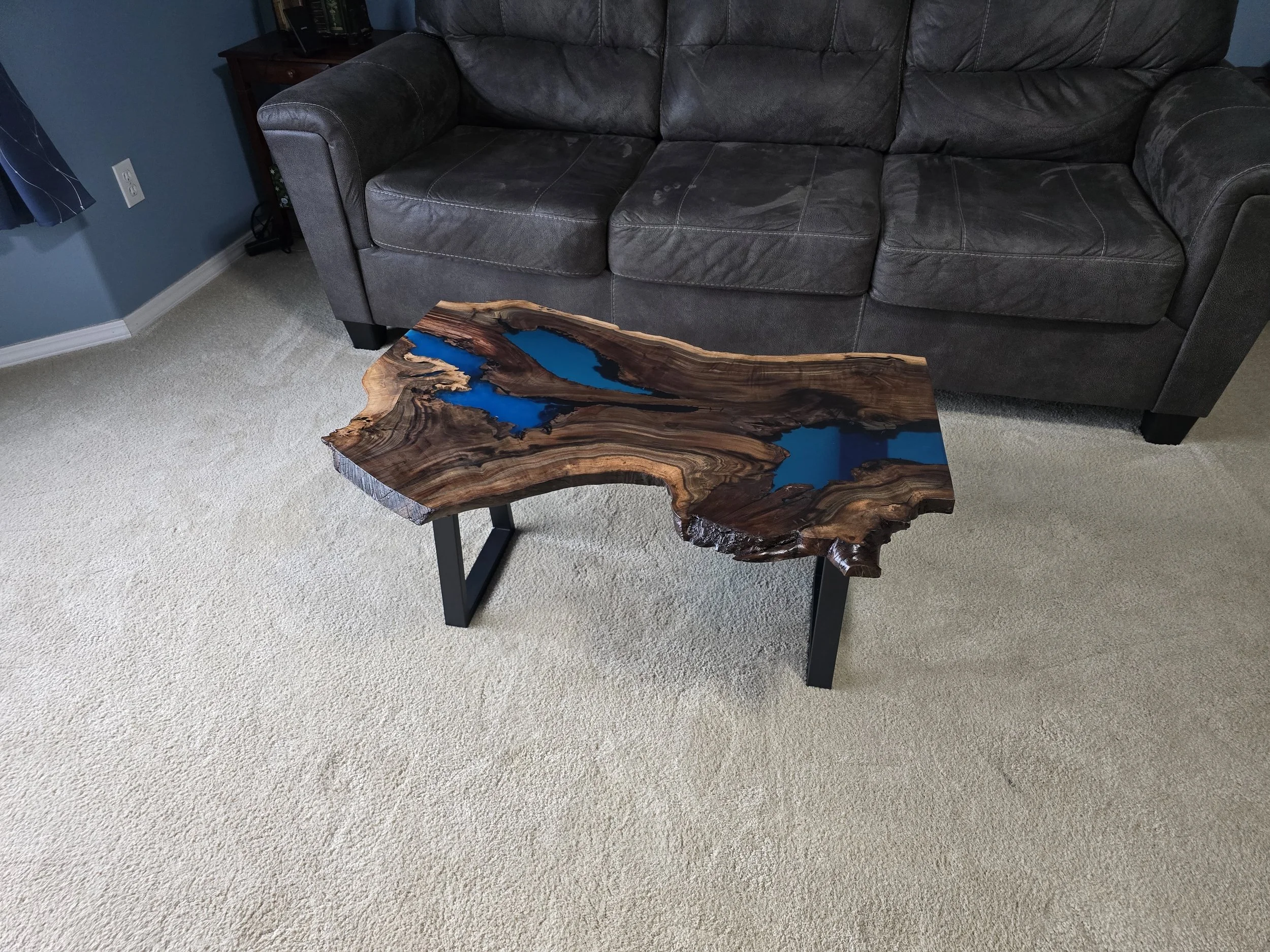 Black walnut coffee table with metal table legs and adjustable feet. Semitransparent blue epoxy fills voids. Measures 18 inches tall, 36 inches long, and 24 inches wide.