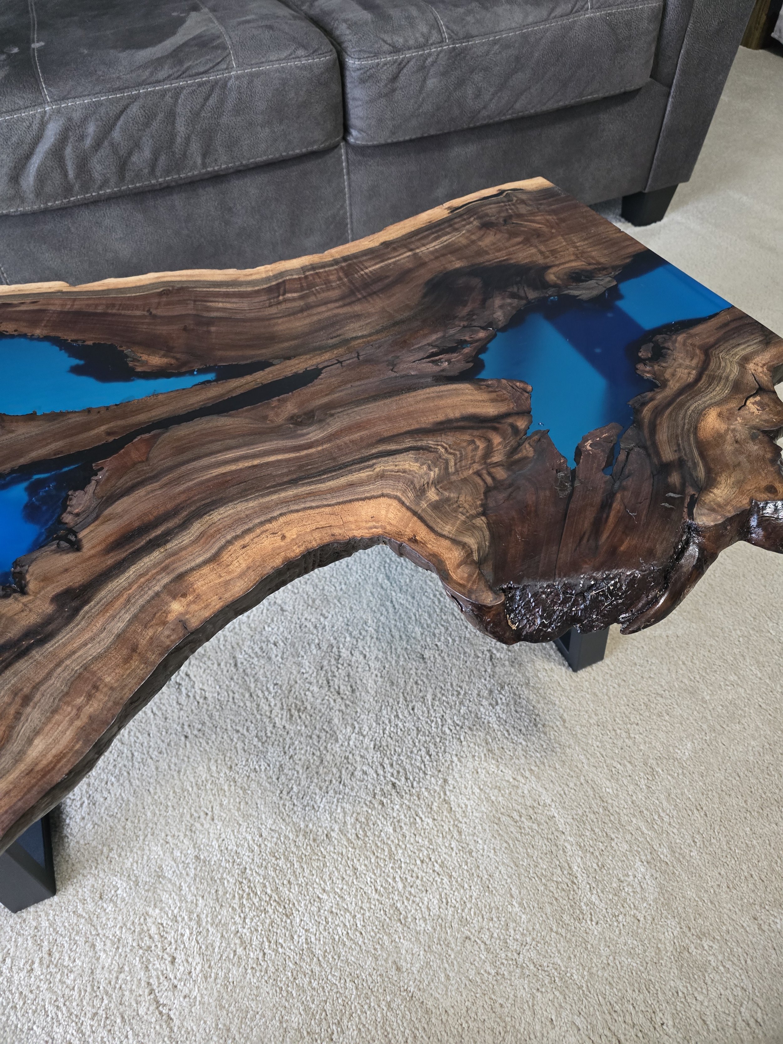 Black walnut coffee table with metal table legs and adjustable feet. Semitransparent blue epoxy fills voids. Measures 18 inches tall, 36 inches long, and 24 inches wide.