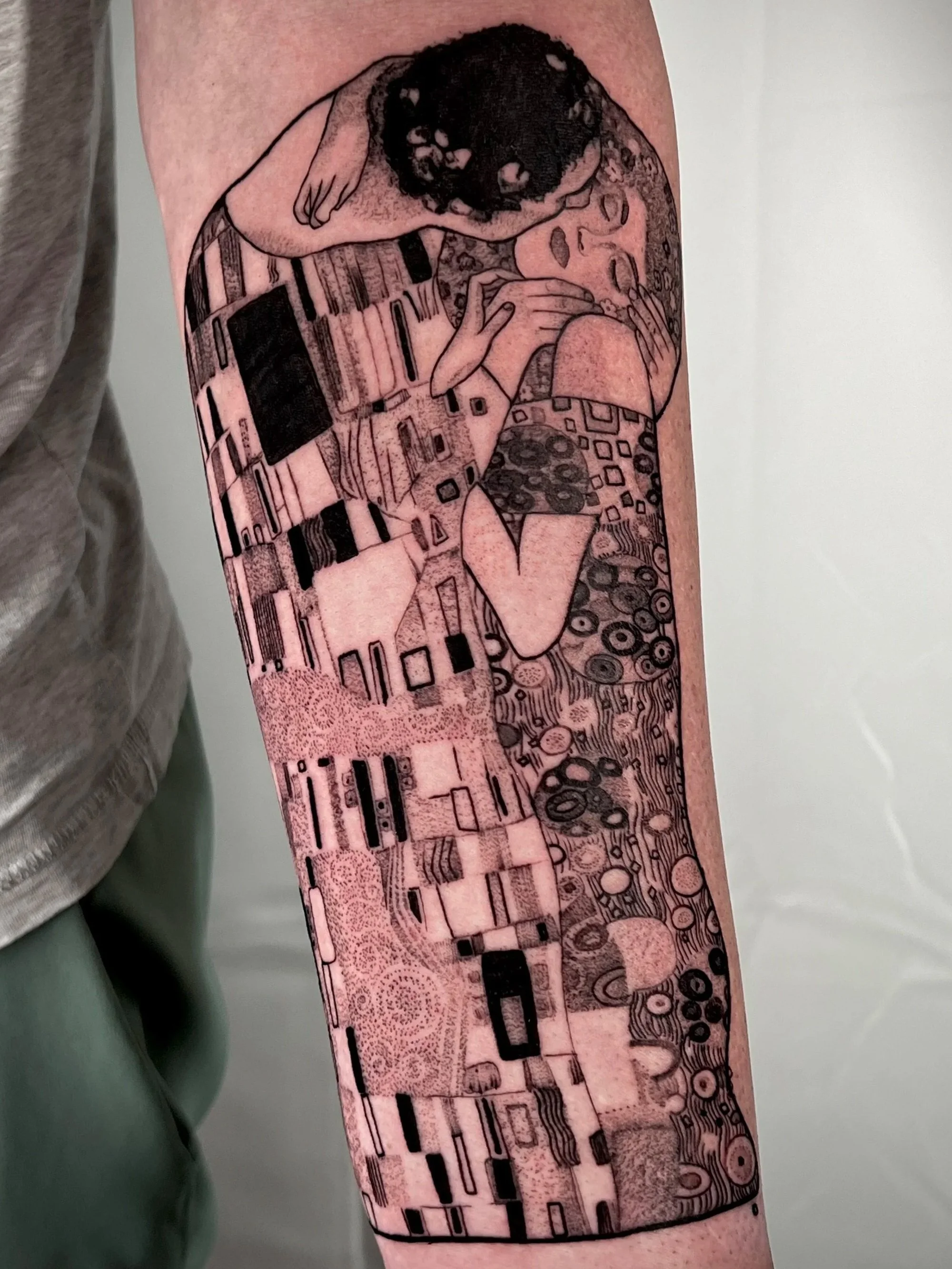 Tattoo of a loving embrace between a man and a woman on a person's arm, with detailed linework and patterns.