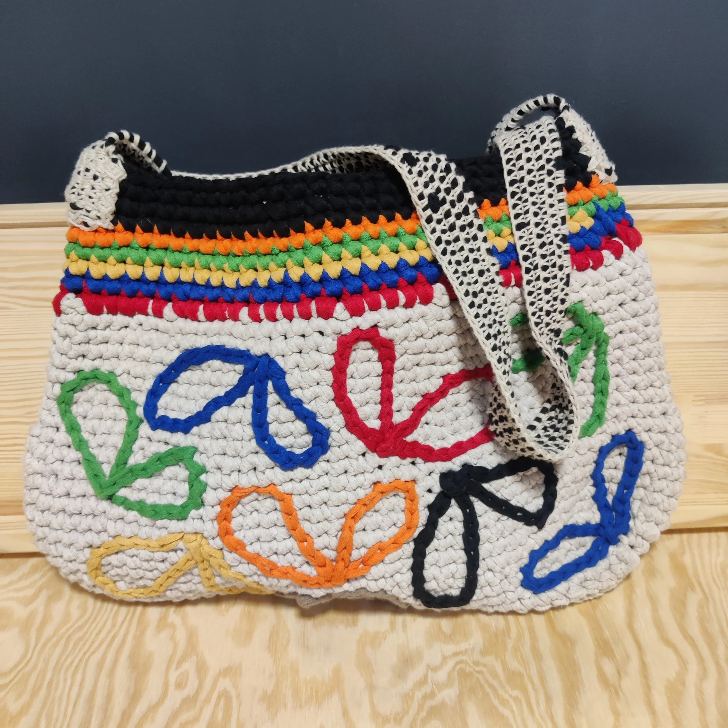 Bolso tejido de crochet el algodón natural con borde superior multicolor y decoraciones de lazo en diferentes colores en la parte frontal.