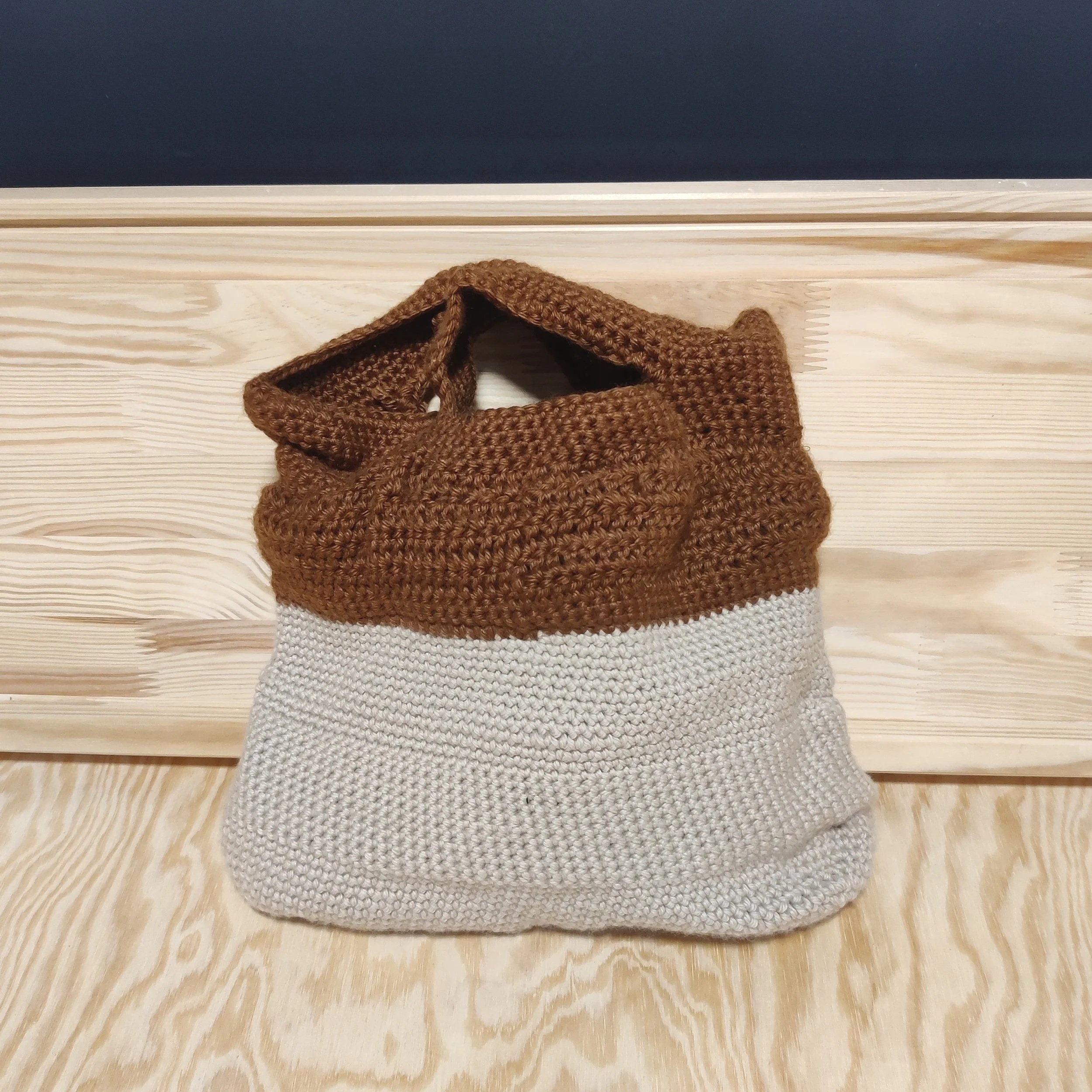 Bolsa de lana tejida en tonos marrón y gris, colocada sobre madera clara.